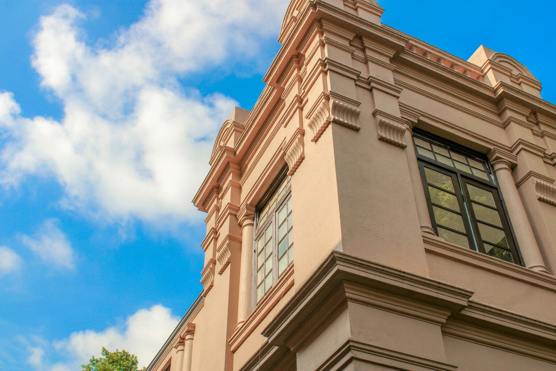 The cornice and tall windows of a classical school building against a blue sky.